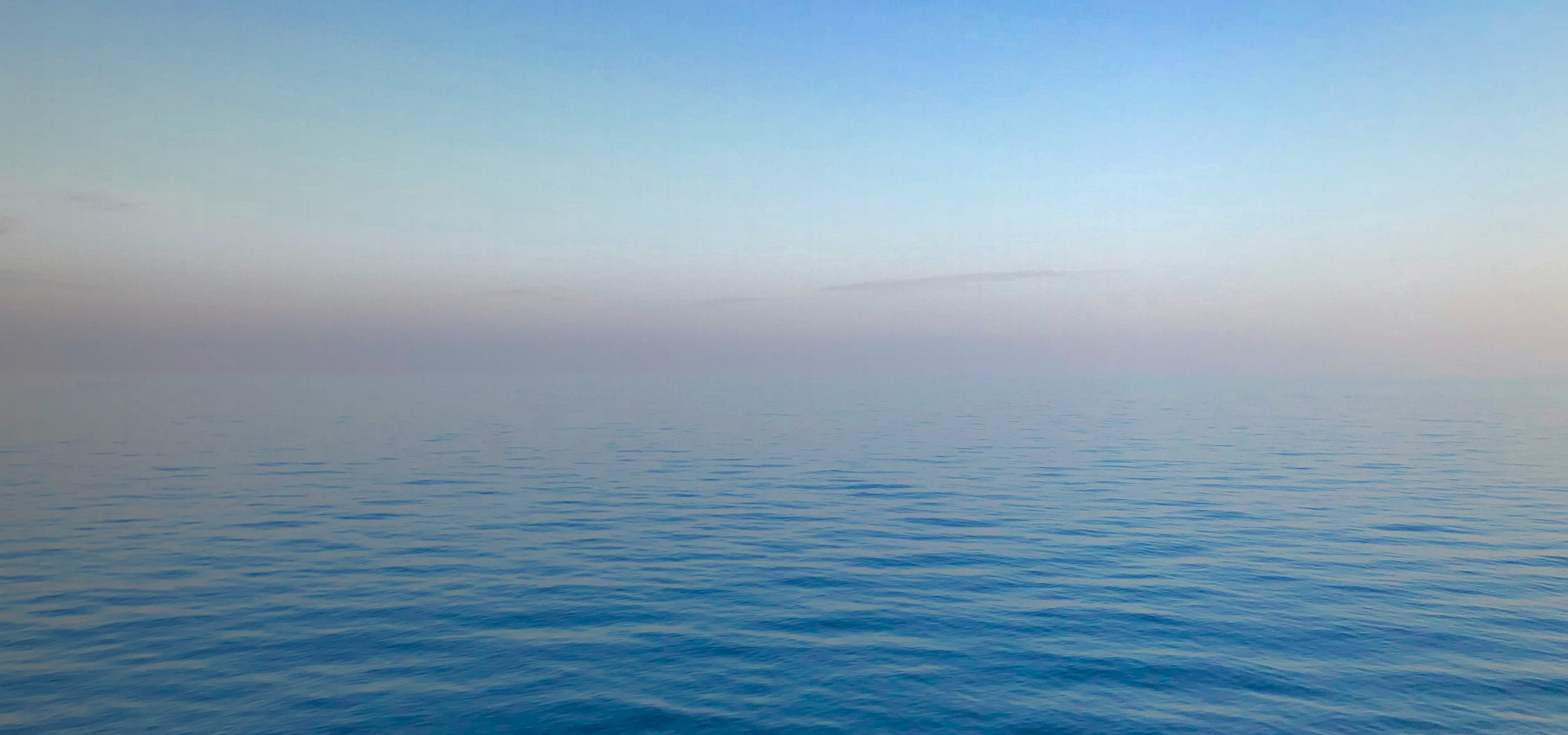 Layers of blue and pink on the horizon over a body of blue water.